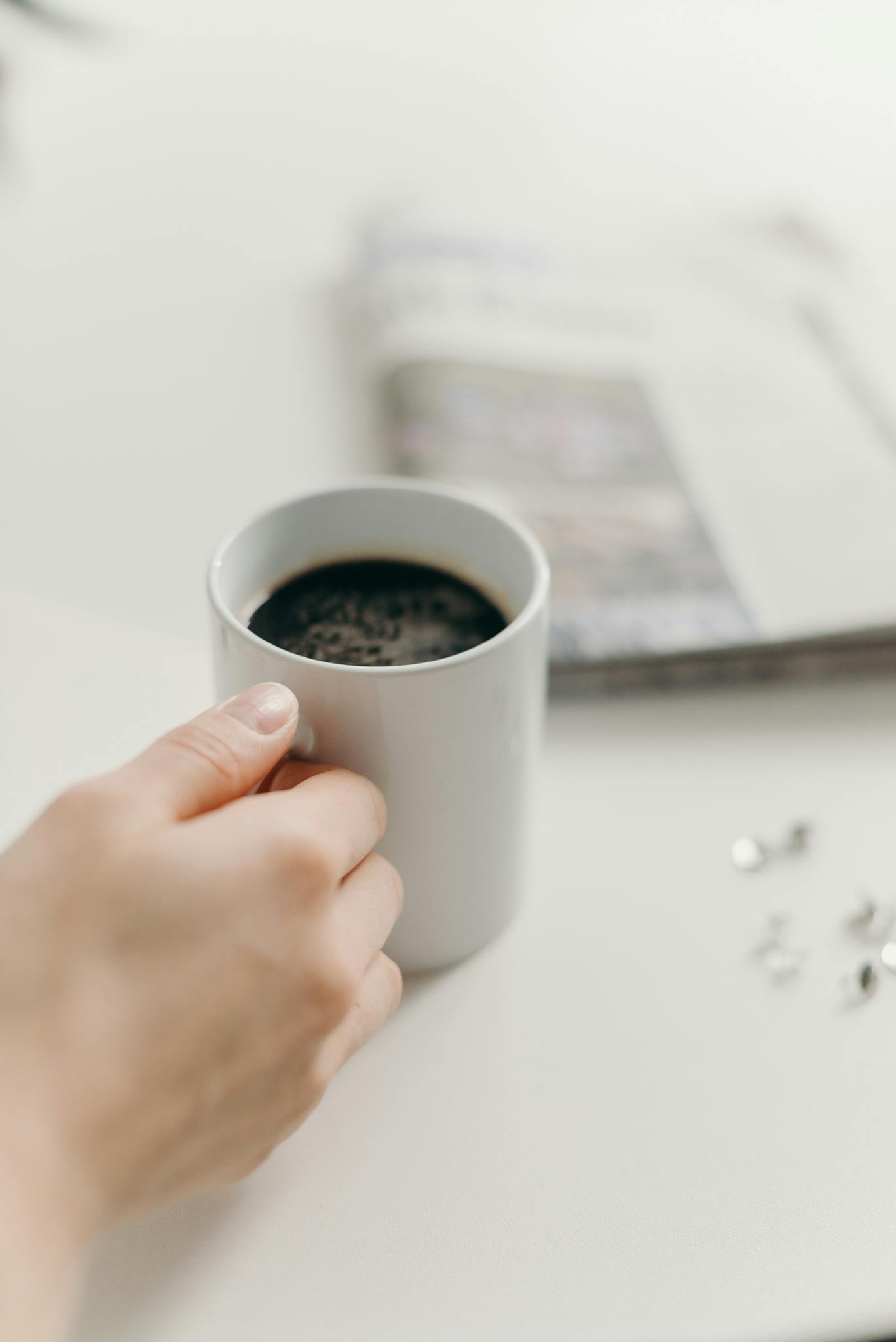 Minimalist close-up of a hand holding a ceramic coffee mug on a white table.